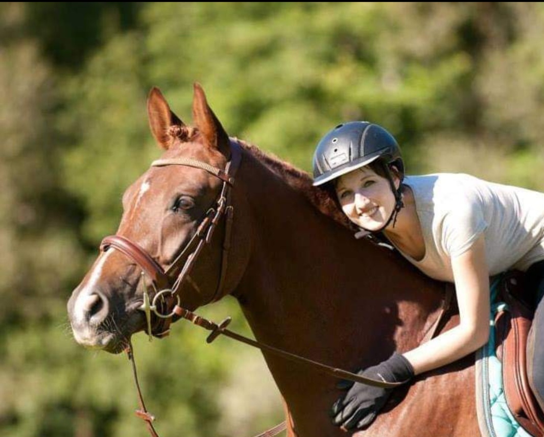 Reiterin mit Pferd Eine junge Frau mit einem Helm umarmt ein braunes Pferd, beide lächeln in die Kamera.